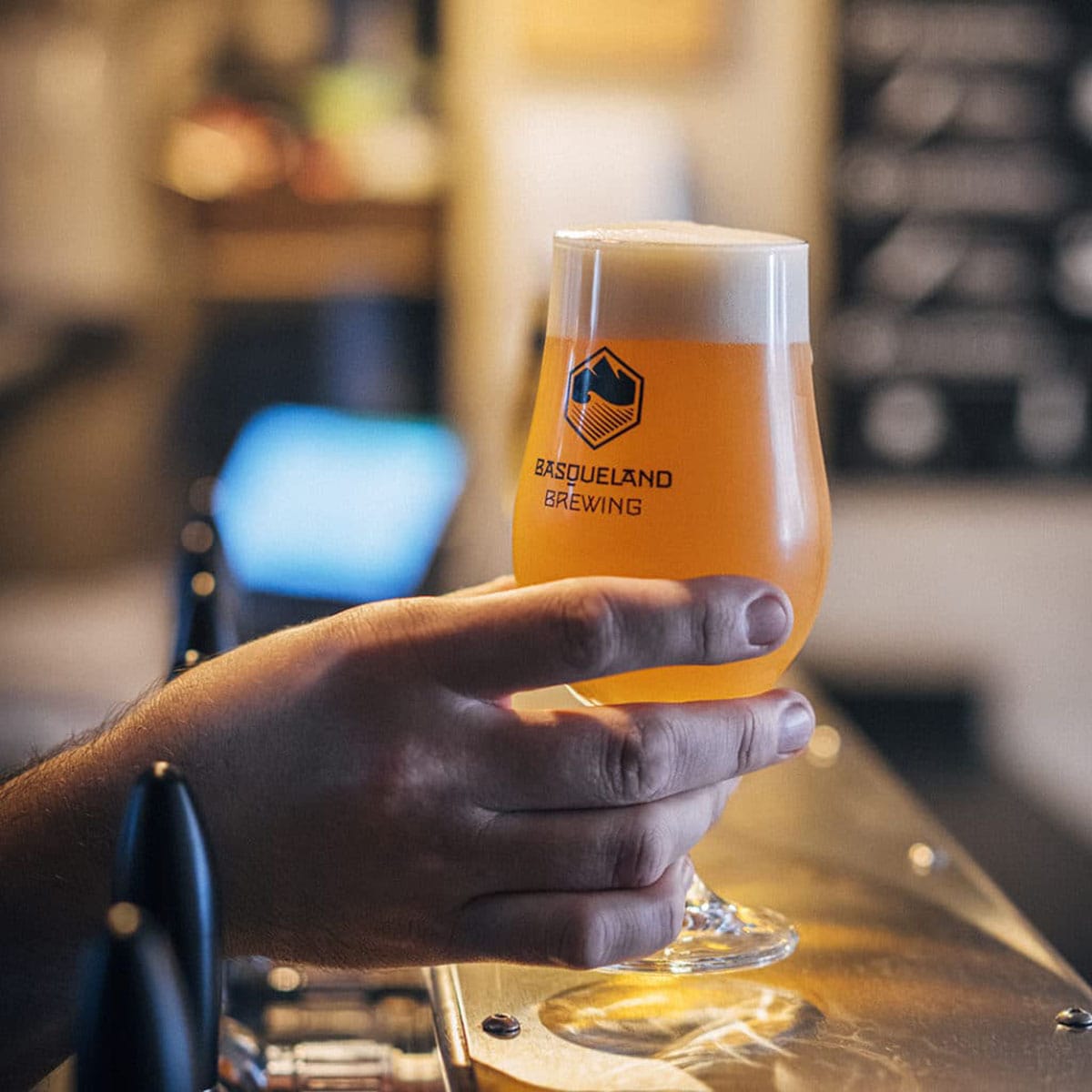 person holding a stemmed glass of draft beer at a bar.
