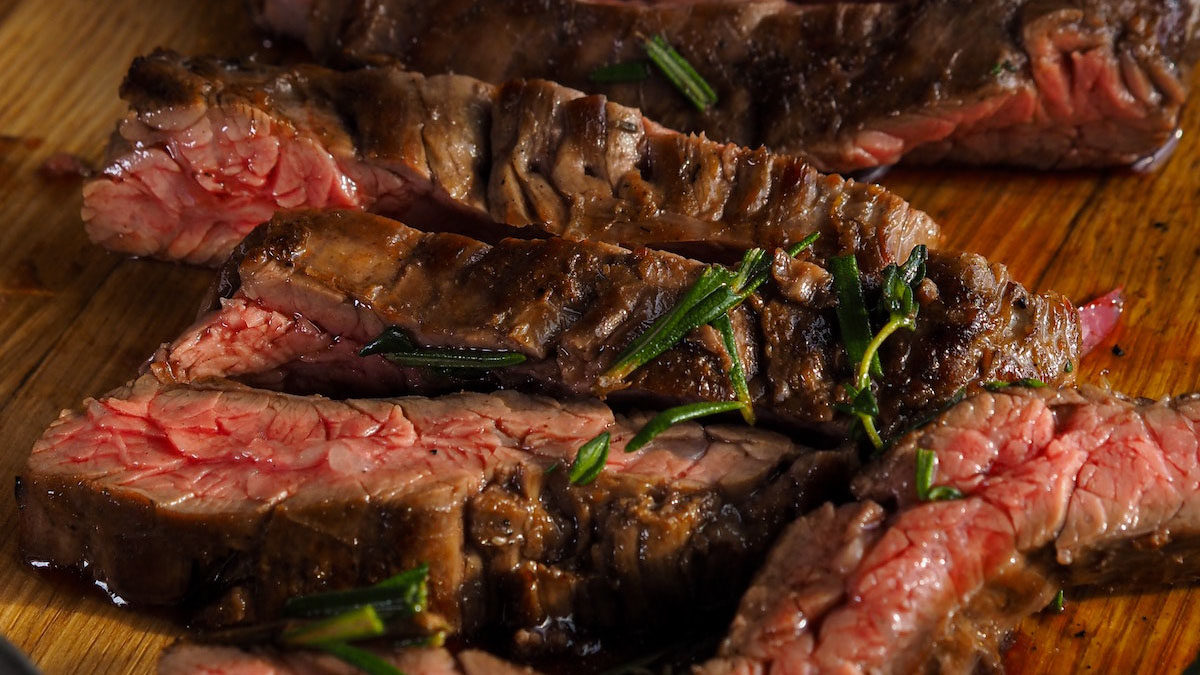 sliced rare steak on a cutting board garnished with rosemary.