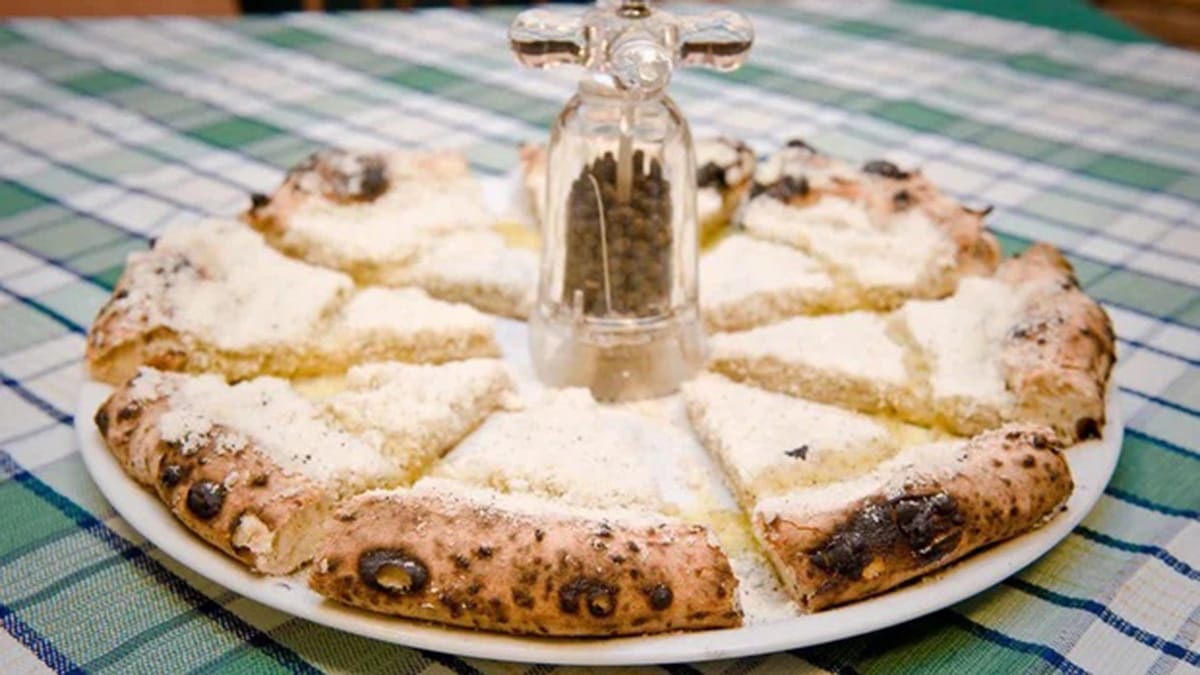 sliced cacio e pepe pizza with a pepper grinder in the center of the plate.