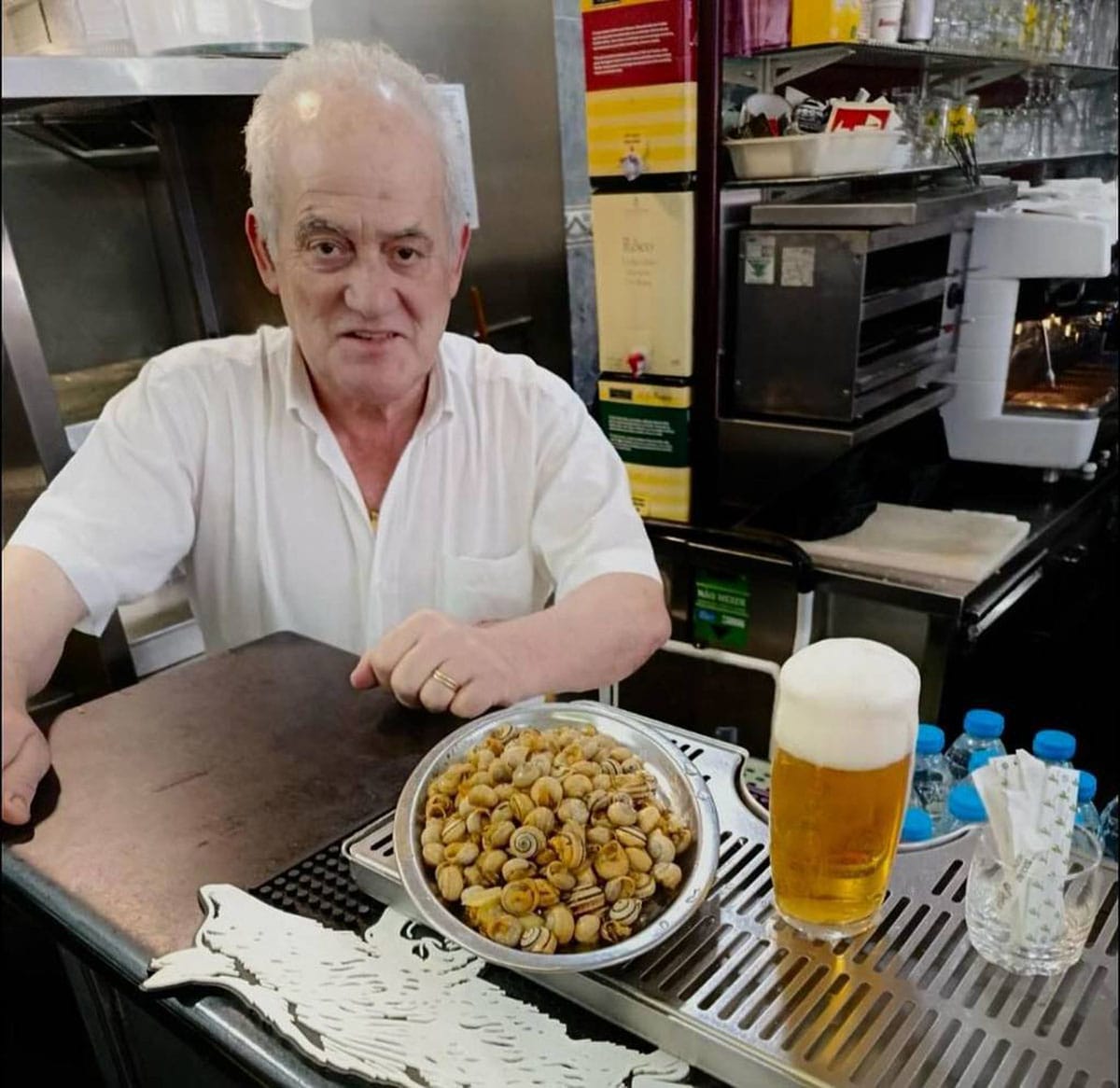 man with a bowl of cooked Portuguese snails and a glass of beer.