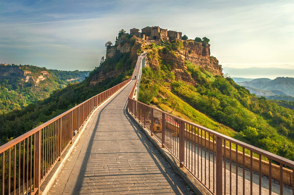 historic city built on top of a rocky and grassy hill with a long footbridge leading to the top.
