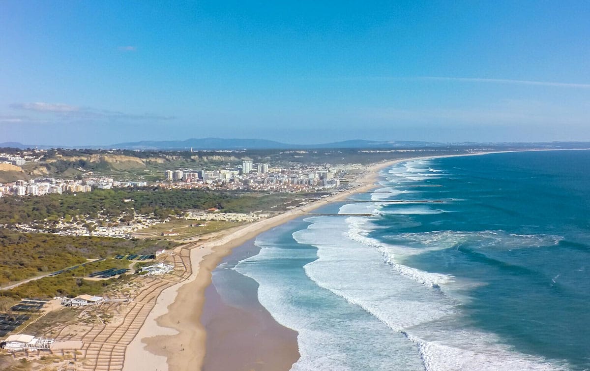 long, sandy beach with blue ocean waves and a nearby city.