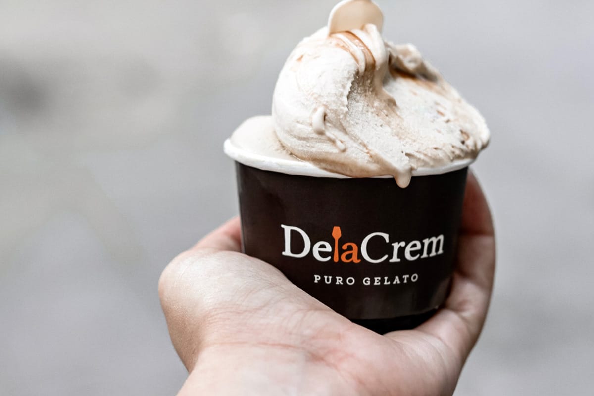 person holding a paper cup of gelato with a wooden paddle.