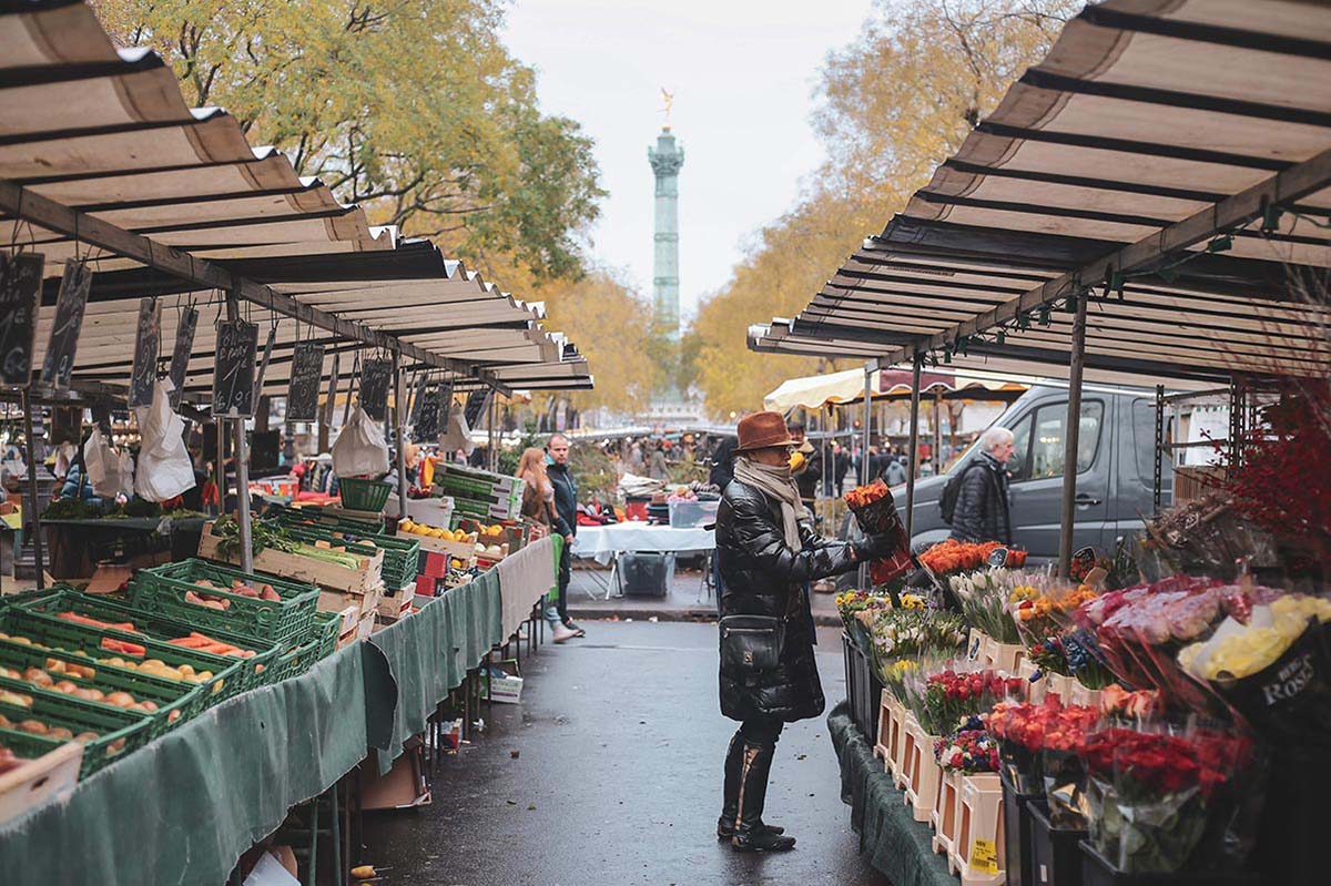 person in a hat, coat, and scarf buying a flower bouquet at an outdoor market in Paris.