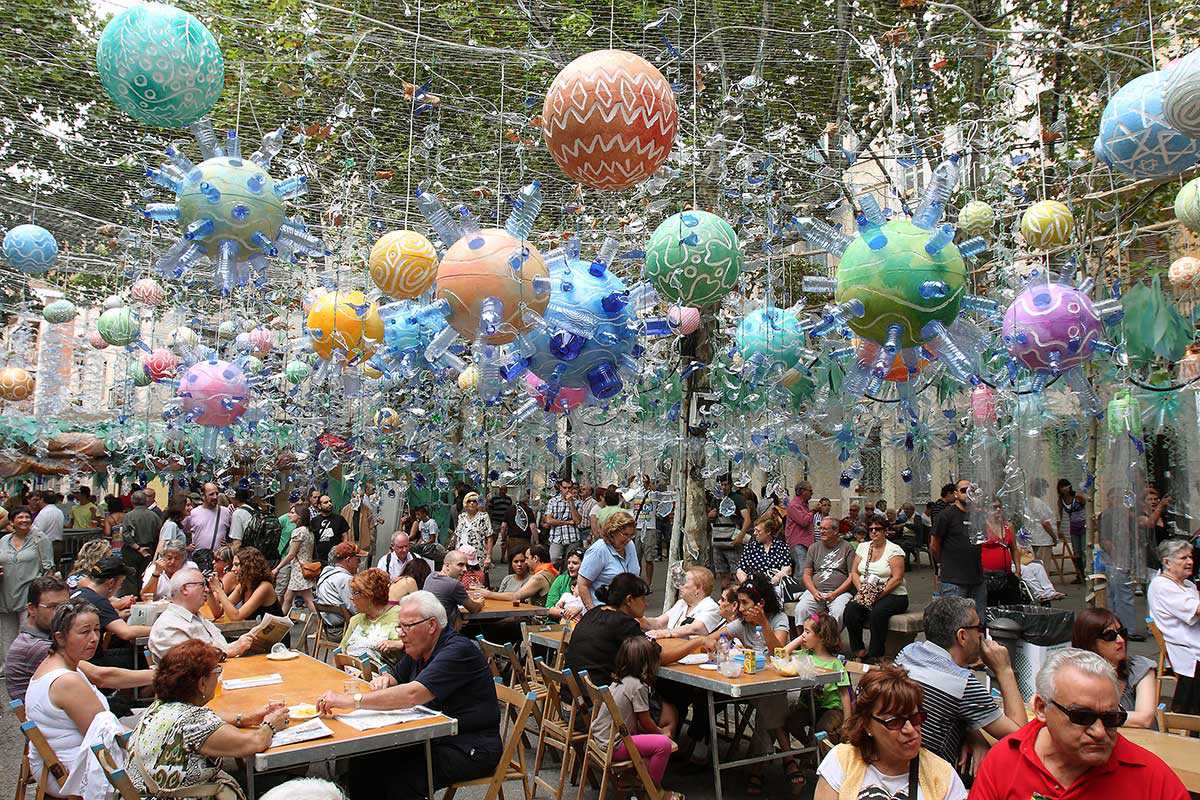 colorful ball-shaped street decorations hanging from mesh over the heads of people sitting and eating at tables.