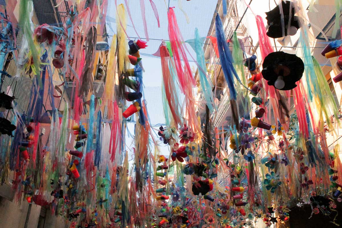 looking up at banners of colorful ribbons and cups strung across a street.