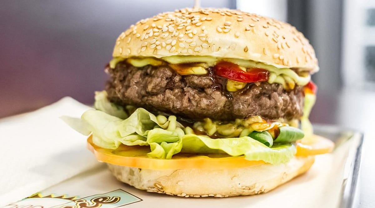 thick hamburger patty in a buns with lettuce, tomato, and other toppings.