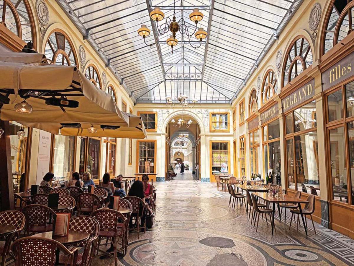 people eating at tables and chairs at a cafe in a covered passageway.