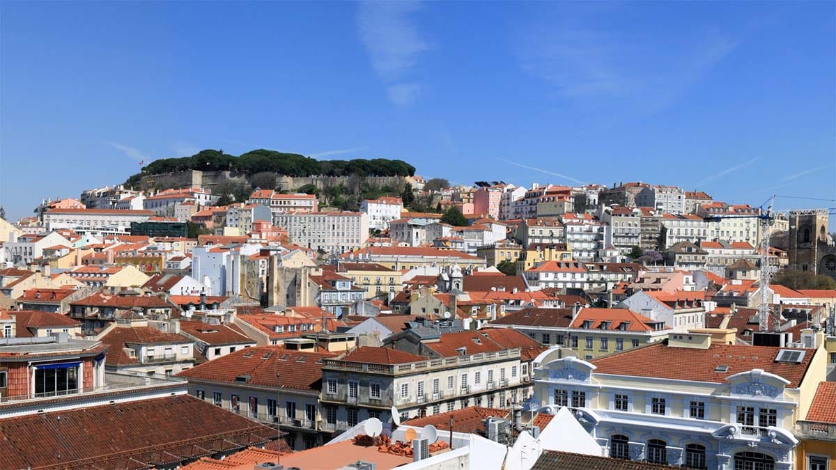 panoramic view of Lisbon's rooftops and castle under a bright blue sky.
