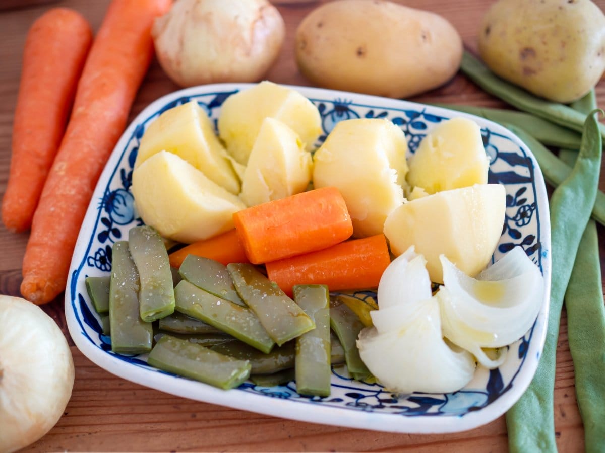 blue and white plate filled with boiled potatoes, onions, carrots, and green beans.