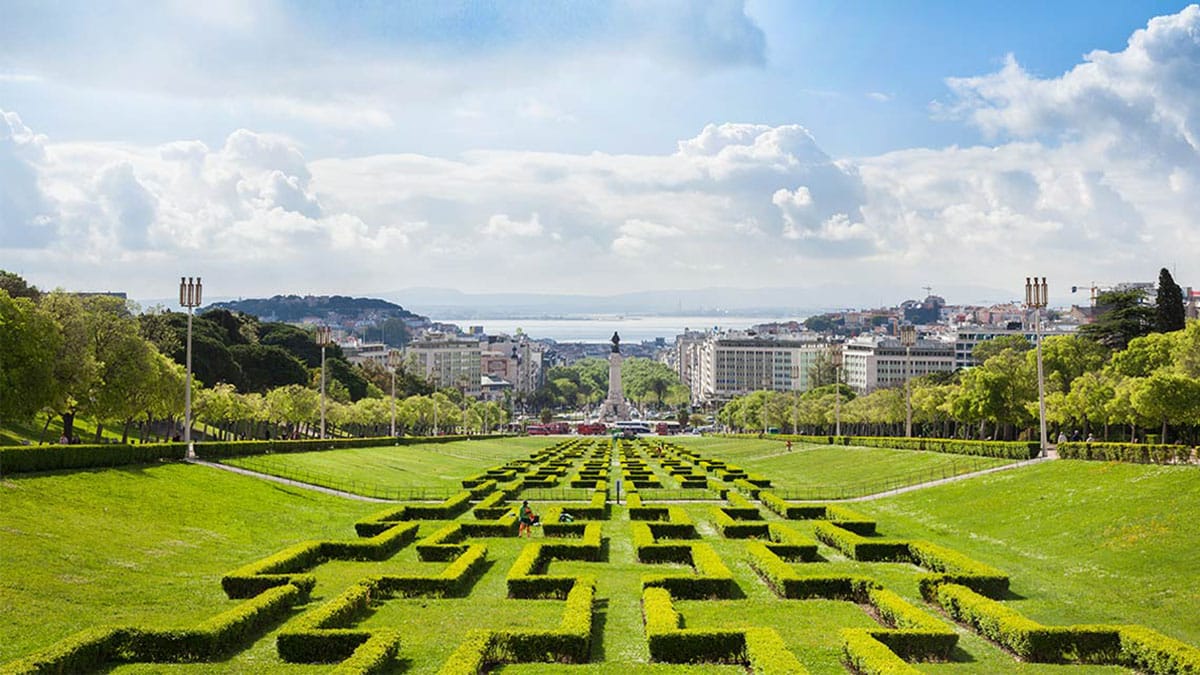 geometrical hedges along a long strip of grass surrounded by trees and the city of Lisbon.