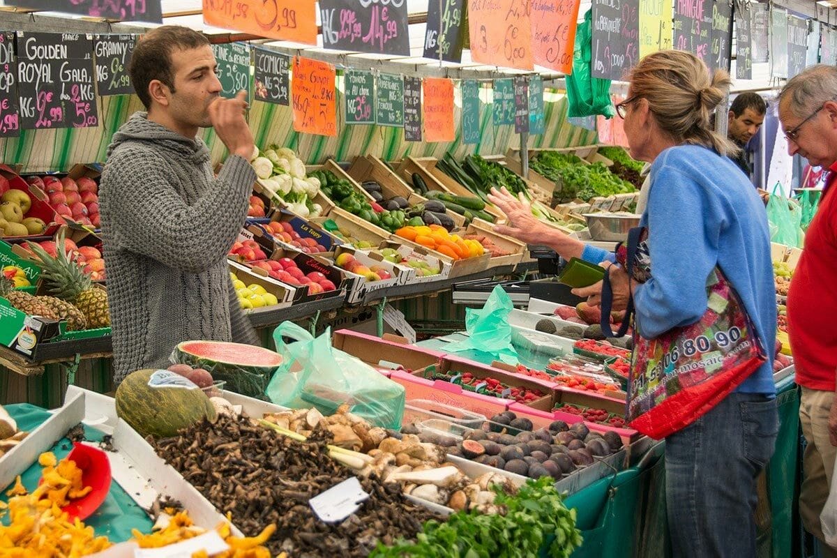 man and woman browsing produce and talking to a vendor at an outdoor farmer's market in Paris.