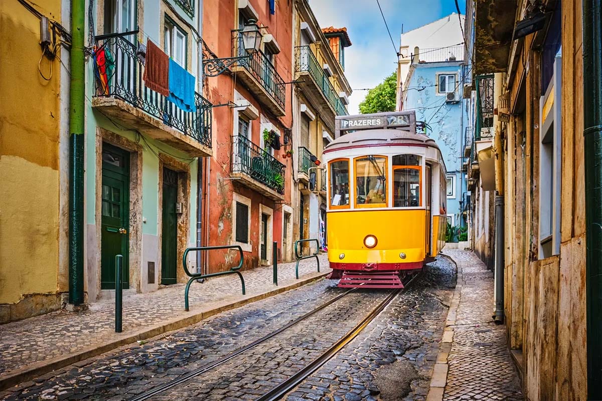 yellow tram 28 in Lisbon on a narrow stone street surrounded by colorful buildings.