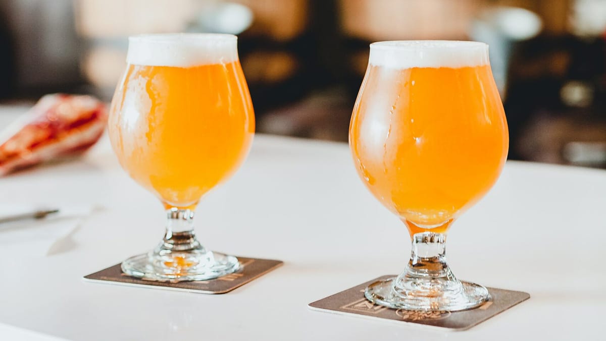 two stemmed glasses of craft beer on a white countertop.