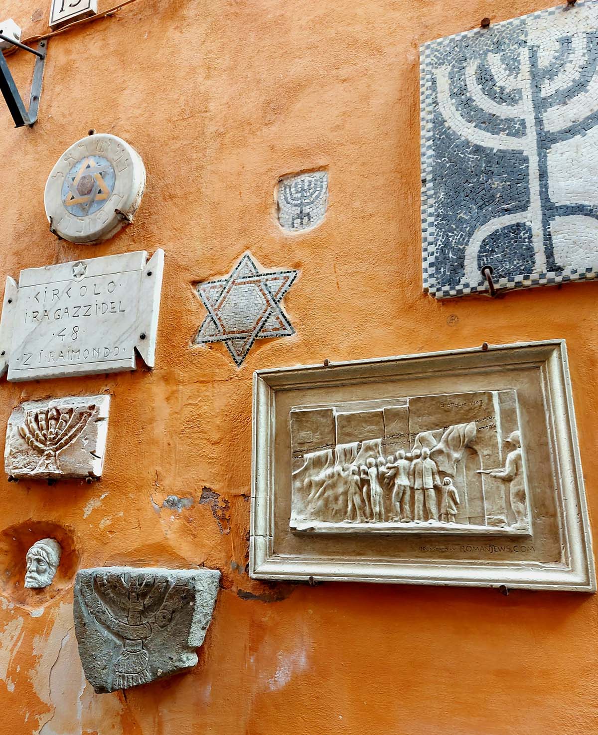 relief sculpture and other Jewish artwork on an orange stucco wall in Rome.