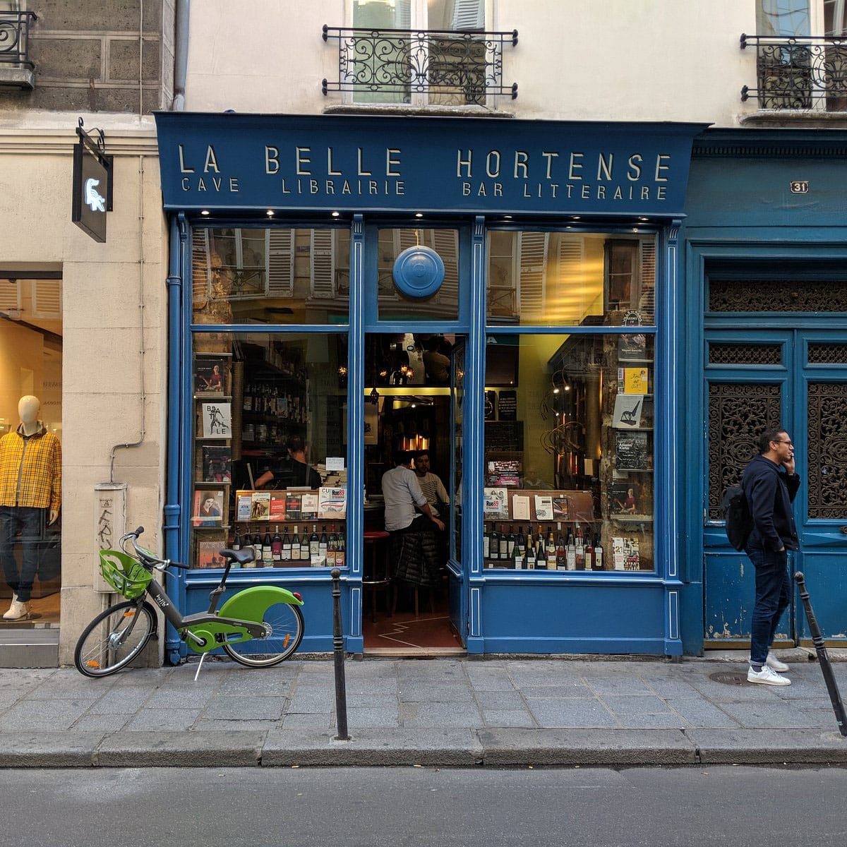 small blue bookstore with glass windows overlooking a sidewalk.