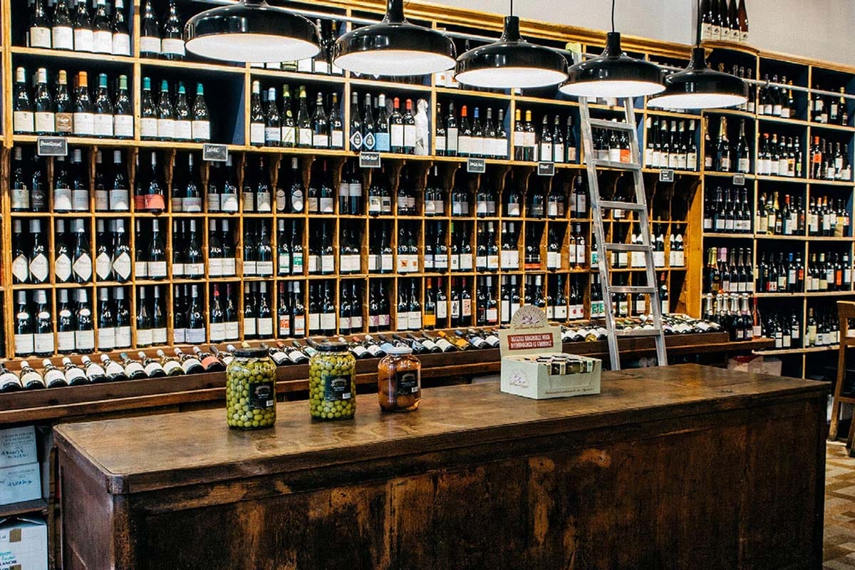 shelves of wine bottles behind a counter with jars of olives.