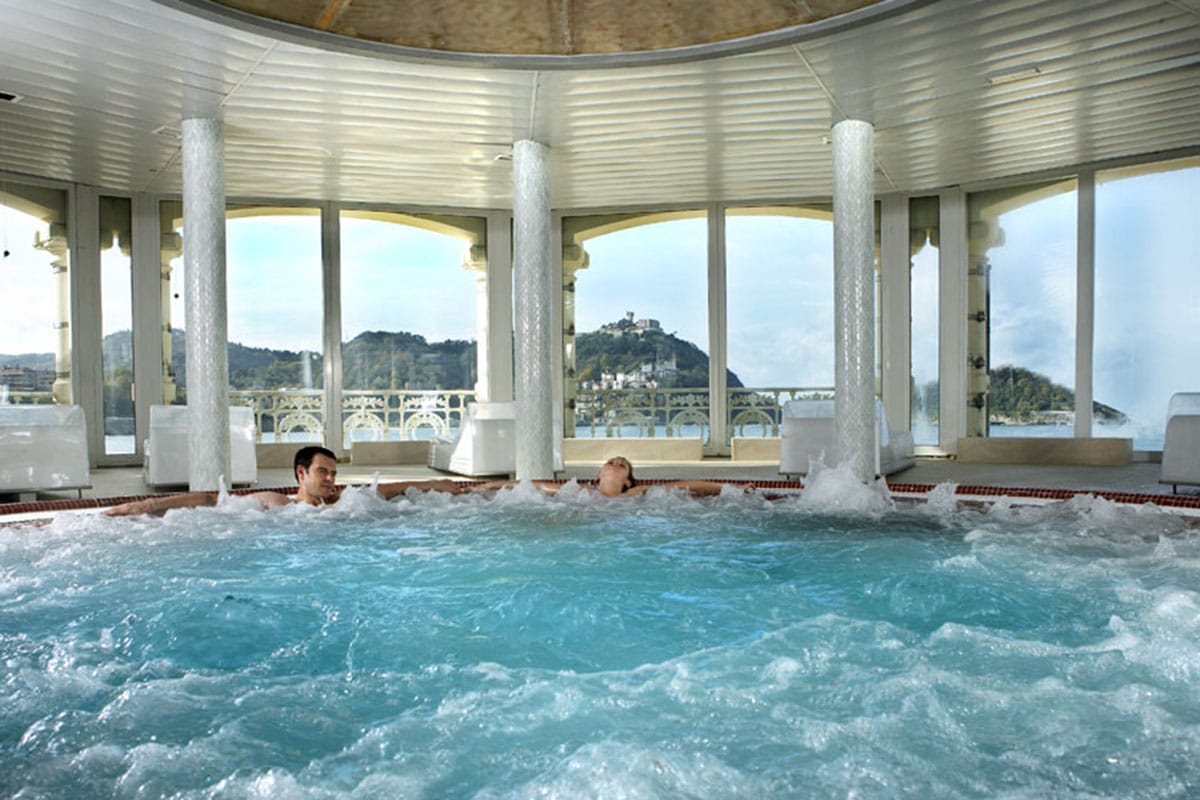 two people relaxing in a large jet pool overlooking the ocean.