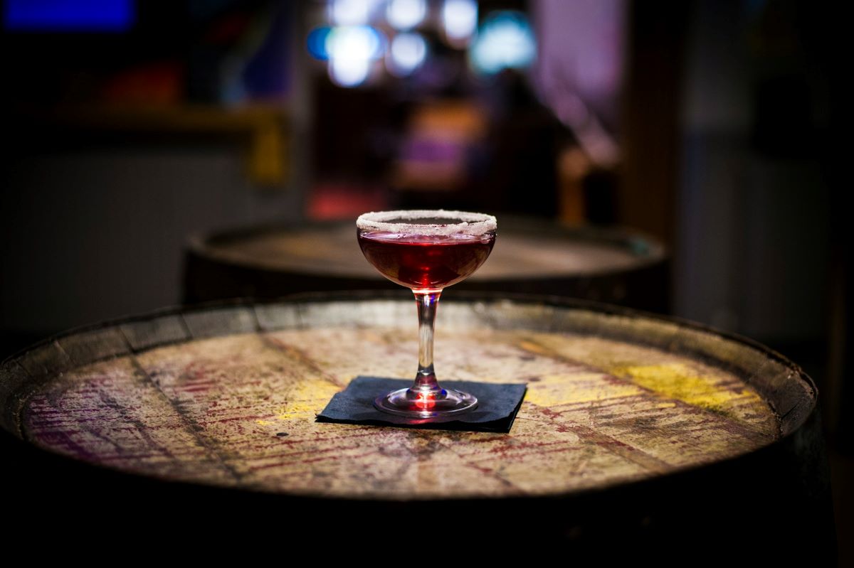 A specialty cocktail resting on a wooden barrel at a speakeasy bar.