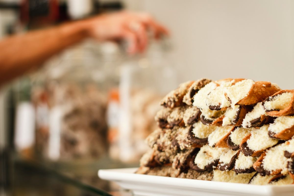 A stack of cannoli as a person behind reaches for other baked goods. 