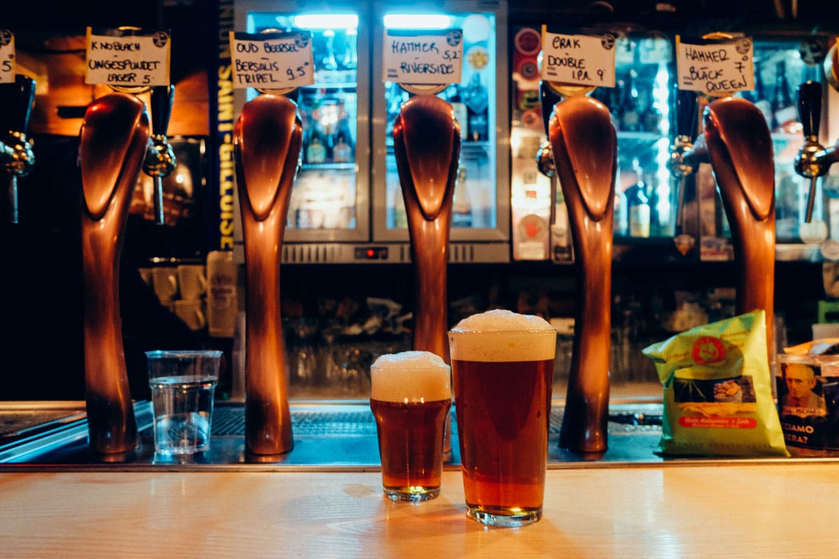 two glasses of foamy craft beer on a bar.