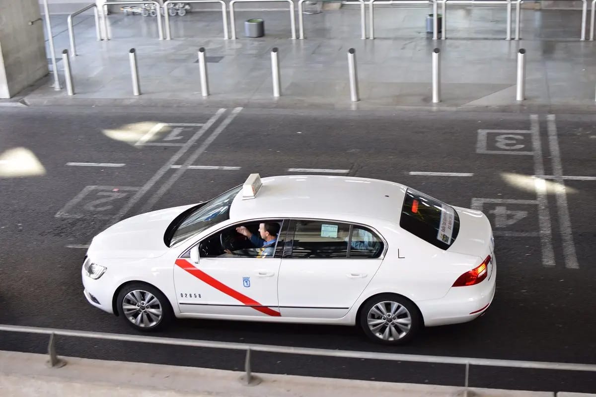 man driving a white taxi with a red diagonal stripe down the front door.