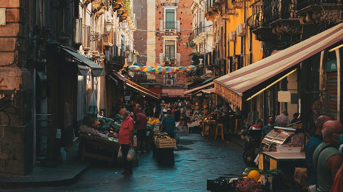 people shopping at food vendors lining a busy city street.