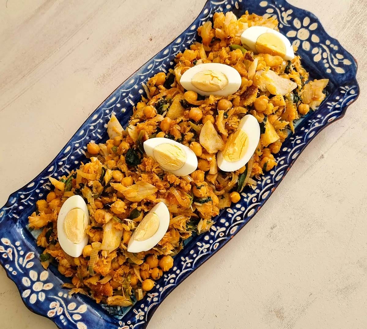 blue and white dish of cod, chickpeas, and hard-boiled eggs.