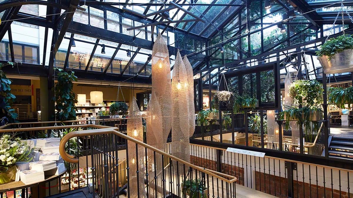 glass-ceilinged store with a chandelier, staircase, and hanging plants.