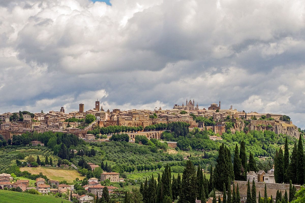 a beautiful historic city on a hilltop surrounded by trees under a cloudy sky.