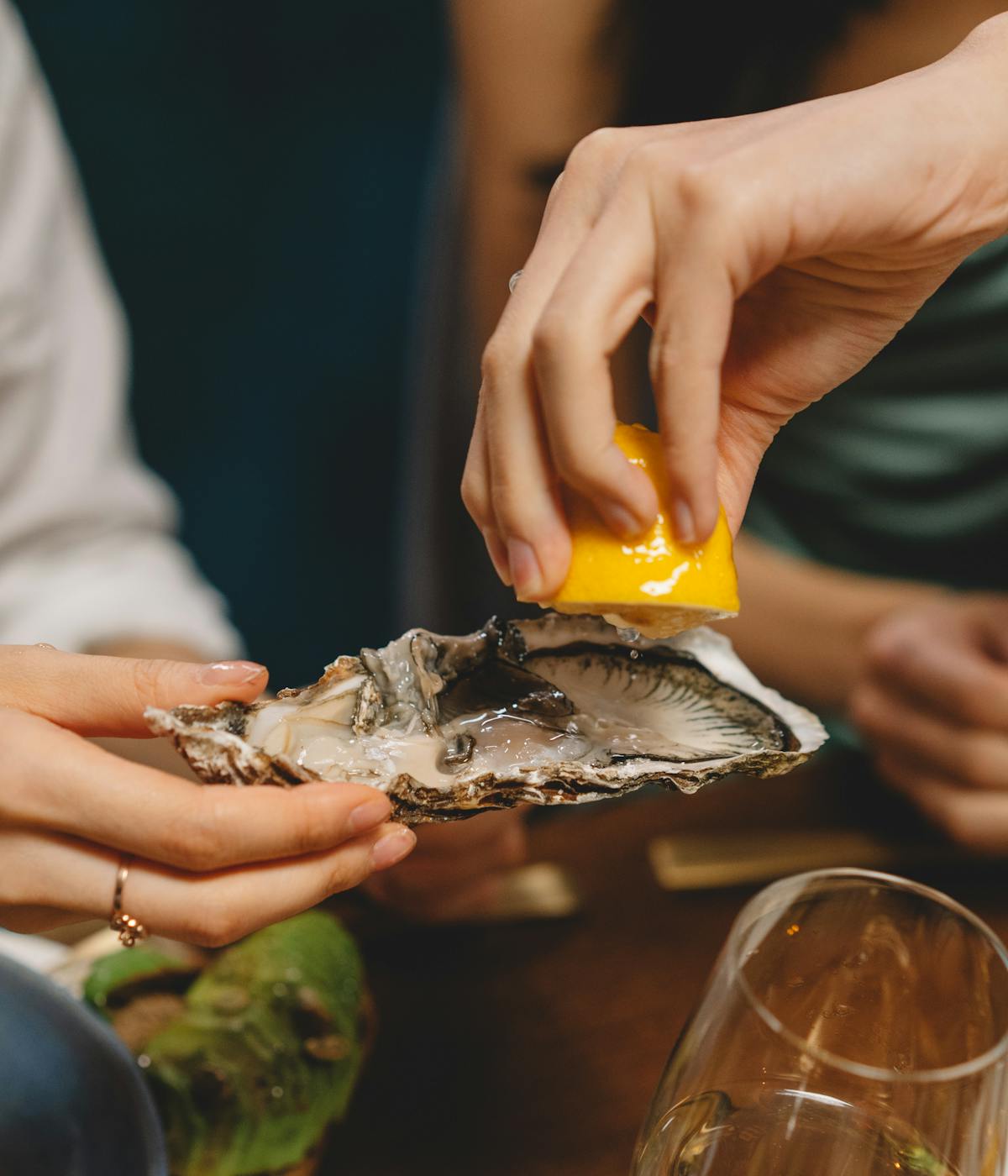 A person squeezing lemon onto an oyster at a restaurant. 