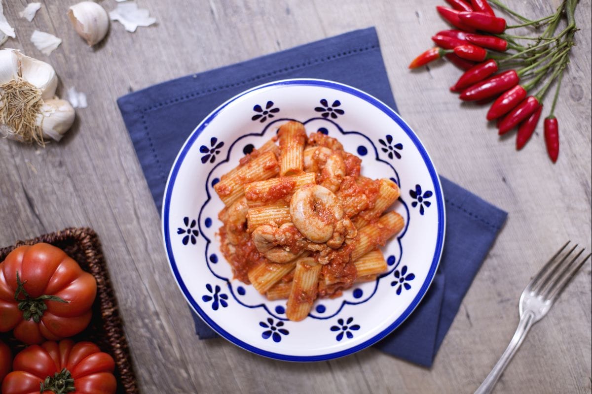 blue and white plate with a plate of rigatoni and intestines in tomato sauce.