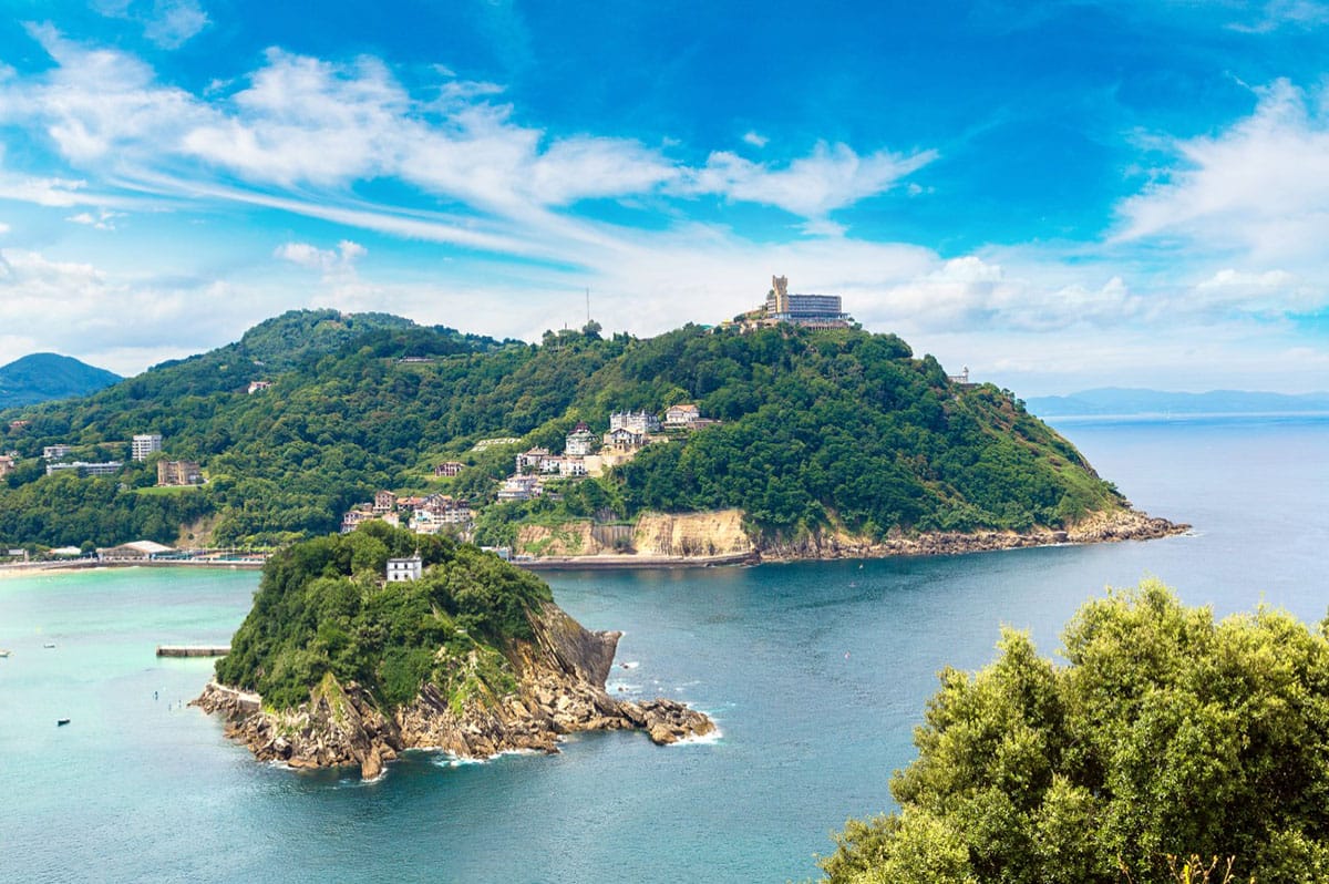 small rocky island surrounded by tree-covered bay and a city.