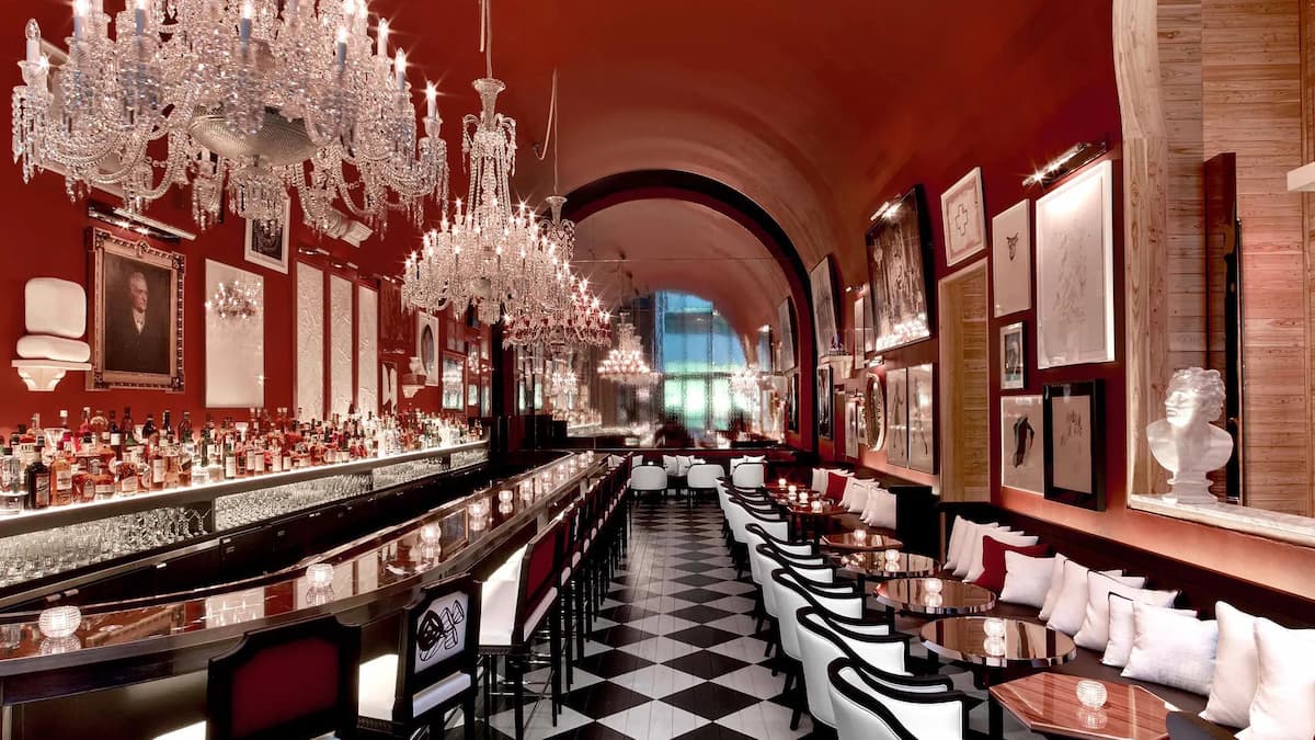 bar with stools and a checkered floor, red walls, and multiple crystal chandeliers.