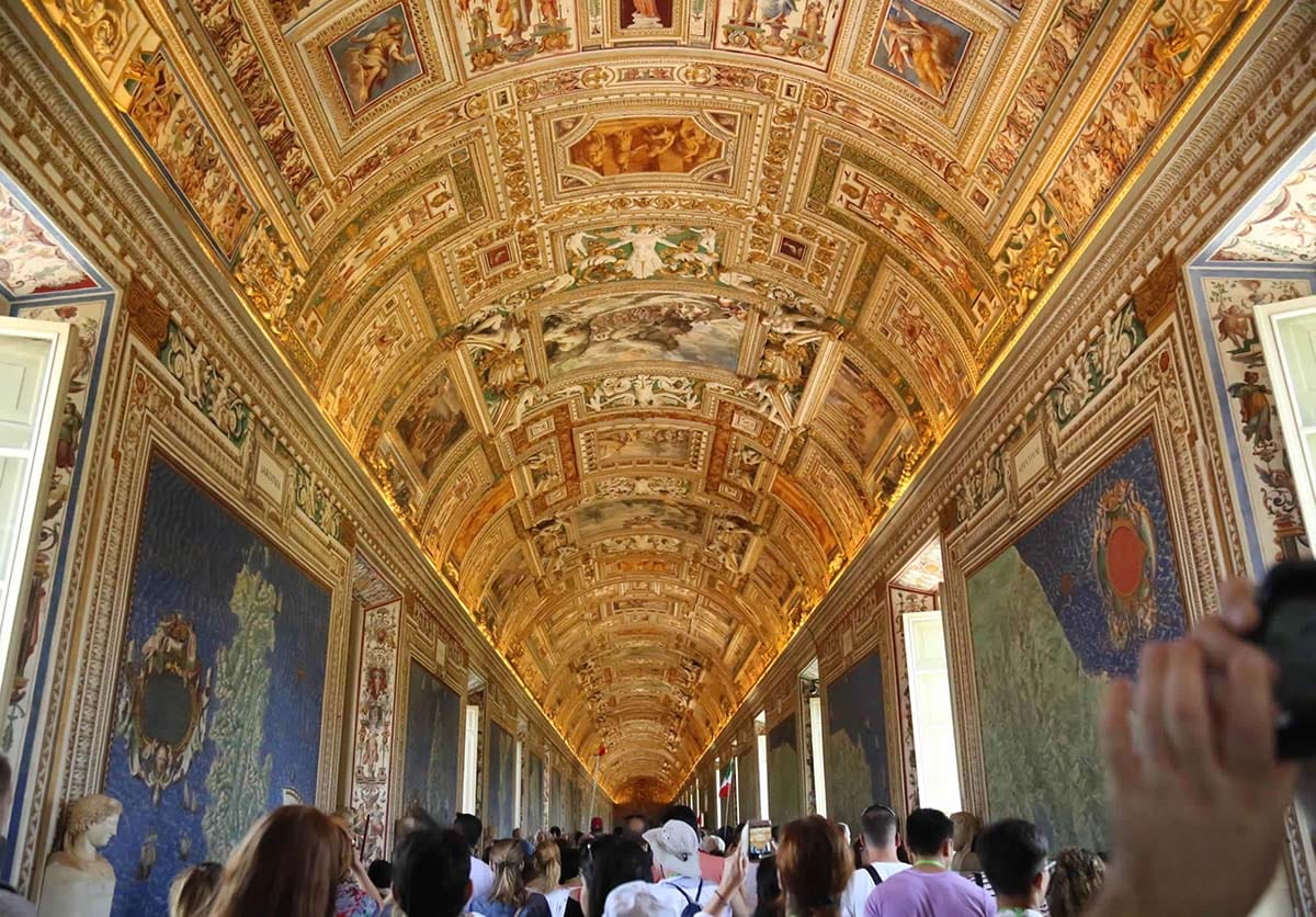hallway of tourists in the Vatican examining famous maps on the walls.